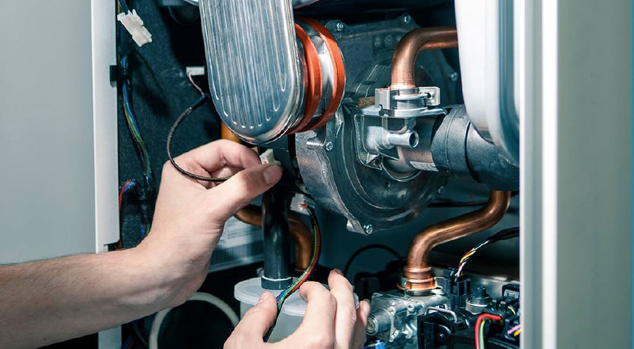 Technician repairing internal components of a gas boiler — copper pipework and wiring